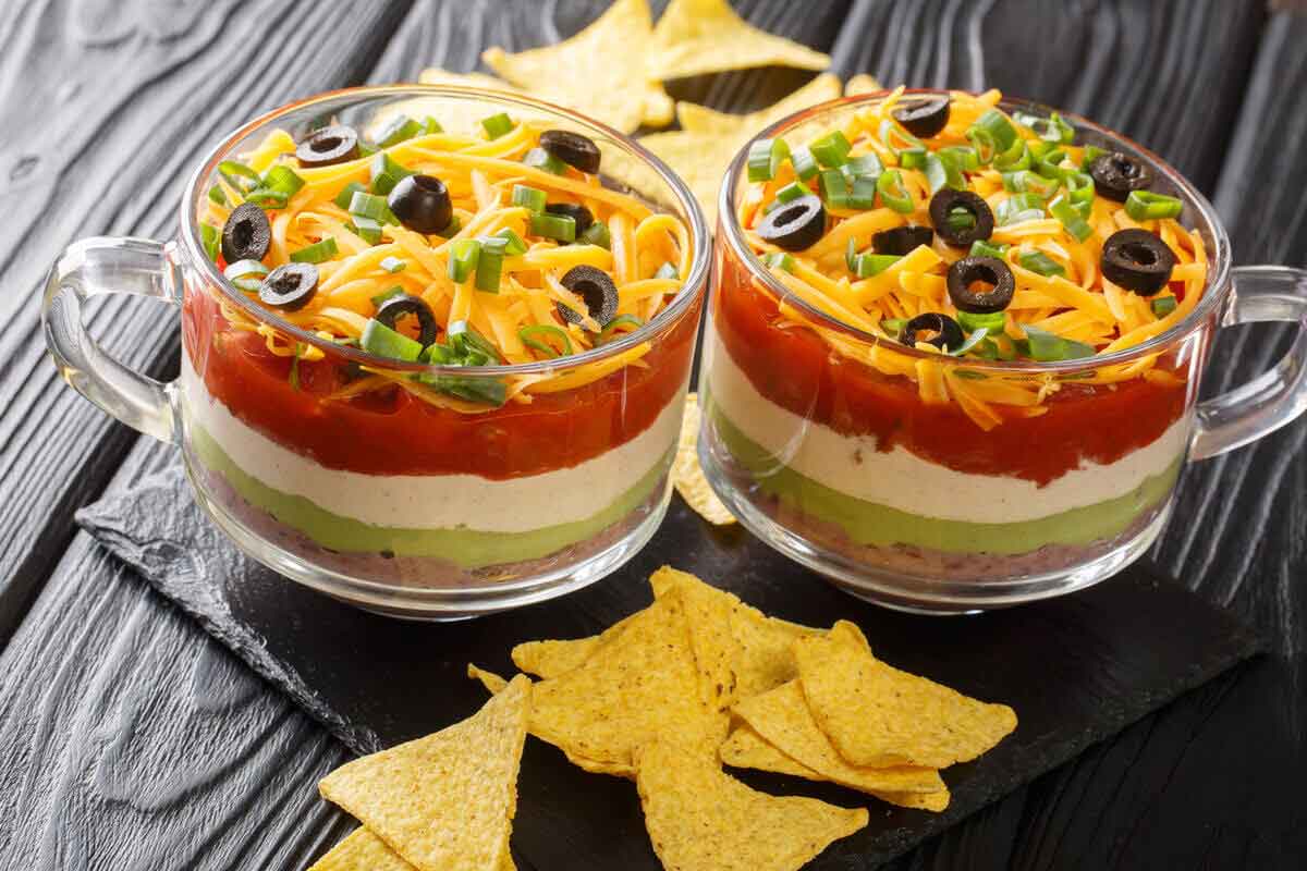 Layered taco dip with refried beans, sour cream, guacamole, salsa, and cheese